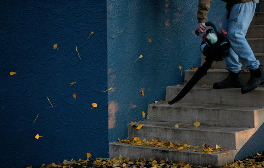 Spring Cleaning for Fire Safety: Is Your Property Ready? A man air-blowing dry leaves off of his property for spring cleaning to protect his house from wildfires.