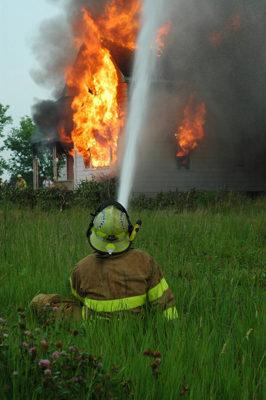 Fire Preparedness Isn’t Optional: How FF1 Helps You Defend Your Home. A picture showing a fireman hosing down a house on fire by spraying it with water from a fire hose.
